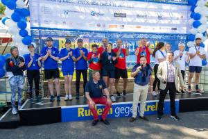 Personen in zwei Reihen bei der Siegerehrung vor der großen Leinwand Benefizregatta "Rudern gegen Krebs"